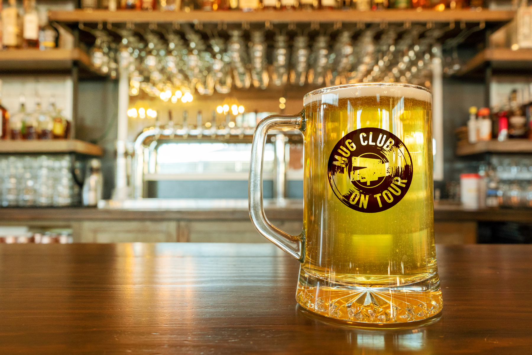 photo of mug of beer on bar with mug club on tour logo on the glass